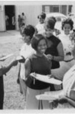 Education leaders hand out materials to young women. Written on verso: Project leaders distribute registration materials to young voters. Rev. Paul McDaniel, Mrs. Charlene Tilley [?].