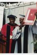 Hank Aaron holds up an award, with Thomas W. Cole, Jr., at the podium at commencement.