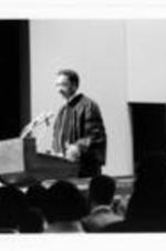 Rev. Jesse Jackson stands behind a podium and addresses a crowd.