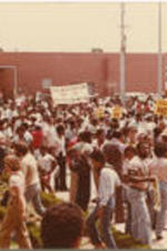 A crowd of demonstrators is gathered for a march in support of Tommy Lee Hines, holding signs and banners that read "Justice Now" and "Self-Determination For The Afro-American Nation".