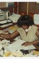 A woman takes a phone call behind a desk.
