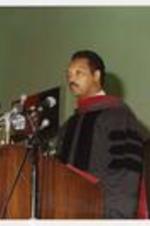 Jesse Jackson stands at a podium and spekas at a commencement.