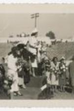 Outdoor view of women standing on podium with bouquets on a football field.