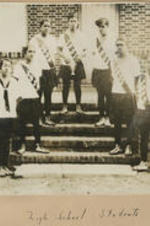 A group of girls stand on the steps wearing sashes and exercise outfits.