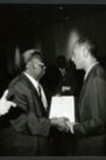 C. Eric Lincoln accepts an award from an unidentified man as L. Henry Whelchel and others look on.