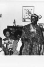 An unidentified man in traditional African dress stands in a living room.