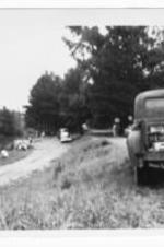 A pick-up truck and several other vehicles are parked on an embankment by a lake.