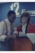 Indoor view of man and woman. Written on verso: "Ronald Fudge '83, TV 12 Eyewitnesses News Anchor, Augusta GA, Class of 1983".
