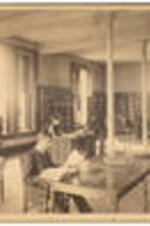 Interior of the Graves Library in Stone Hall with male students looking at books while a woman sits at a desk.