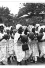 Women walk together in a group playing Shekeres.