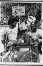 Participants of the "We Are Doing It" Walkathon to support disability rights are shown in their wheelchairs holding protest signs.
