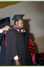 An unidentified faculty member places a red hood on a graduate.