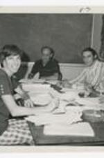 Three men and two women sit around a table covered with papers in a classroom.