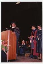 Lou Rawls stands at a podium while Thomas W. Cole, Jr. and a woman stand behind him laughing.