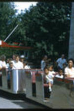 Anna Henderson and children with unidentified people on a tourist train at an amusement park.