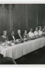 Indoor view of people seated at tables. Written on verso: L to R, Mr. H.S. Murphy, Miss Dingle, Class 11, Dr. Frederick A. Jaeboch, Class 24, Dr. C.R. Yates, Class 20, Mrs. Yates, Class 15, Mrs. Murphy, '09, Dr. Williams, '16, Mrs. Bridge Williams, '12, Dr. Robert Barton Jackson, Class '14, Dr. Paul Clifford.