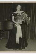 Camilla Williams holding a bouquet of flowers with a piano in the background.