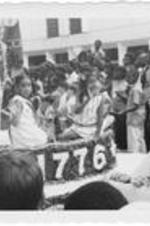 Two girls wave to the crowd while riding on the Vine City parade float. Written on accompanying document: Part of Vine City's float.