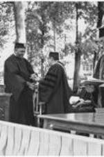 Dr. Harry V. Richardson (background right) presents a degree to John Moulton.