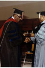 An unidentified man receives his diploma and shakes Dr. Grant Shockley's hand.
