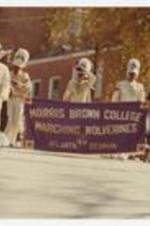 Outdoor view of people wearing marching band uniforms, on banner "Morris Brown College marching Wolverines, Atlanta Georgia".