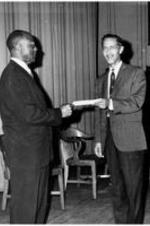 James P. Brawley exchanges a document with another man.