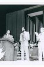 President Hugh Gloster on stage with unidentified persons and Edwin Moses as he holds a plaque.