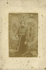 Portrait of a woman standing behind a chair.