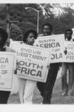Augusta College students and Southern Christian Leadership Conference members are shown holding anti-apartheid signs during a demonstration to protest the performance of a South African boys choir at the college. Written on verso: SCLC Condemns Apartheid -- Black students at a predominantly white Augusta College in Augusta, Georgia stage demonstration with SCLC leaders, including National SCLC President Joseph E. Lowery, to protest a concert appearance there by the Drakensberg Boys Choir of South Africa. The students met with the institution's administration, but the concert was not cancelled. Nevertheless, their opposition reached the ears of the choir's members and much of the American public. A performance scheduled for the choir at the University of Georgia several days before, was cancelled following protests from black students there.