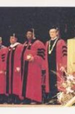 C. Eric Lincoln stands on stage with other unidentified men while receiving an honorary degree from Boston University.