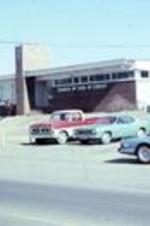 The Church Of God In Christ State Temple of Southwest Arkansas with cars in foreground and man waving at the camera.