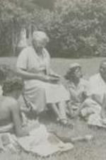 View of unidentified group sitting in the grass around a woman.