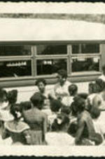 Unidentified children and adults standing beside a school bus.