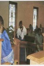 Shy Temple congregation. Written on verso: Kayla-Keys Lewis holds her arms up to her face in front of the congregation.