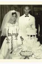 Beth A. Chandler and Theodore John Warren in front of wedding cake at ceremony.