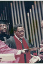 Dr. Wildon Jackson hands a diploma over to Dr. Hugh Gloster to present to Joseph E. Lowery (at center) during Morehouse College's commencement ceremony.