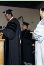 Dr. Grant Shockley stands next to James Costen giving a commencement address to the graduating class.