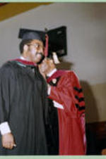 An unidentified graduate crosses the stage in front of a faculty member at a graduation ceremony.