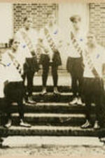 A group of girls wearing sashes and Converse shoes stand on house steps, possibly a track team.