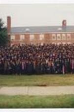 Graduates pose for a large group portrait in front of a brick building at commencement.