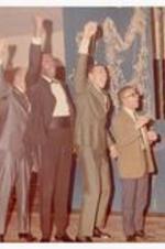 A group of men wearing suits, raising fists into the air.