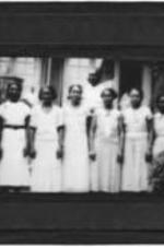 View of an unidentified group of men and women standing outside wearing white.