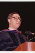 Colin Powell stands at a podium and speaks at the summer commencement.