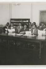 James P. Brawley stands in front of a large table where to a group of young men sit holding booklets.