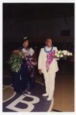 View of man and woman holding bouquets of flowers. Written on verso: "Miss Morris Brown College, Julliette Burgess + Father, Mr. Burgess, Nov. 1987; L to R. Juliette Burgess, Norris Burgess".