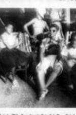A young Ruby D. Smith sits in a chair and poses with a group of people.