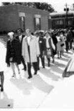 A large unidentified group of people walk in procession in front of a building.