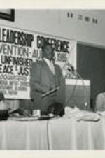 Reverend Fred Shuttlesworth is shown speaking at a podium alongside Joseph and Evelyn Lowery and others during the 28th Annual Southern Christian Leadership Conference Convention. Written on verso: Where it all started... Rev. Fred Shuttlesworth, an SCLC founder and leader of the now famous Birmingham Movement tells "how it was" before SCLC in Alabama.