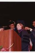 Thomas W. Cole, Jr. and another man adjust the graduation hood of a woman, at the summer commencement.