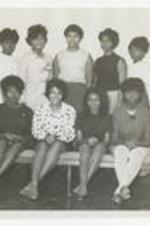 Nine women pose sitting on and standing behind a long bench.
